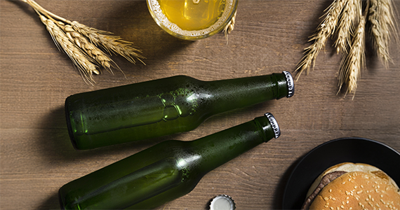 Deux bouteilles de bière allongées avec des branches de blé de chaque côté.